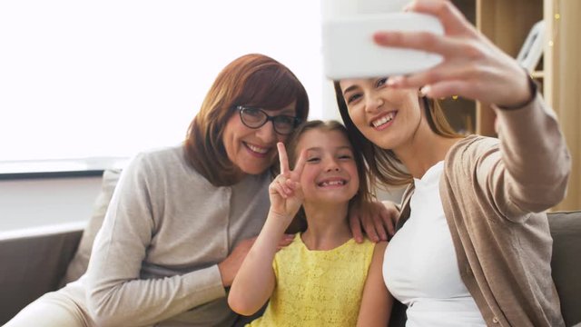 family, three generations and technology concept - happy mother, daughter and grandmother taking selfie by smartphone at home