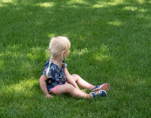 Fototapeta premium Little Caucasian Girl Sitting in Green Grass