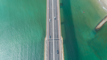 Aerial view of car driving on a bridge with natural forest trees, sand, tropical beach and waves...