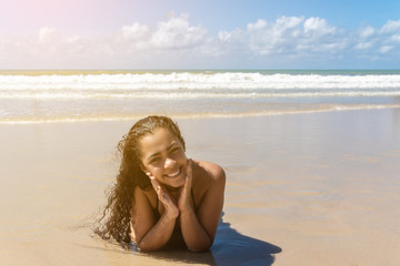 Fototapeta na wymiar Happy healthy beautiful Brazilian multiracial woman lying down on sand enjoying sun tanning sunbathing in swimsuit relaxing on Brazil tropical beach summer vacation. Smiling laughing girl.