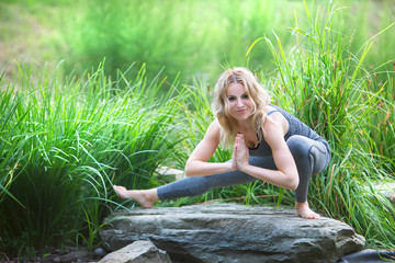 beautiful slim young woman doing yoga sitting on a stone in the park
