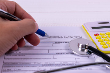 Health insurance concept. Health care costs. Hand holding pen point to medical claim form, Stethoscope and calculator symbol for health care costs or medical insurance.