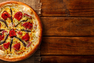 Pizza anchovy and dried tomato on wood background. Top view, close up. Traditional Brazilian Pizza.