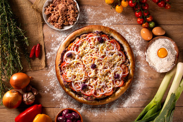 Pizza tuna fish, onion, tomato and black olive on wood background. Top view, close up. Traditional Brazilian Pizza.