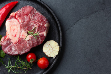 Raw fresh ossobuco con herbs, garlic and chile pepper on black plate. Dark background
