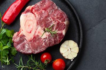 Raw fresh ossobuco con herbs, garlic and chile pepper on black plate. Dark background