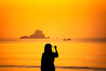 Silhouette of young woman taking pictures of landscape at sunrise.