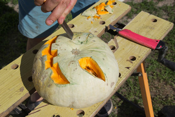 Halloween pumpkin cutting process, process of making Jack-o-lantern. Male hands with knife, leftovers of pumpkin on the kitchen table