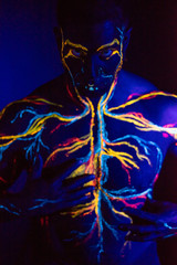 UV picture of the circulatory system body art on the body of an adult male. On the chest of a muscular athlete, veins and arteries are drawn with fluorescent dyes. Neon light.