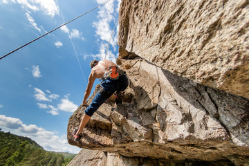 Climber Extreme climbs a rock on a rope with the top insurance, against the blue sky, bottom view