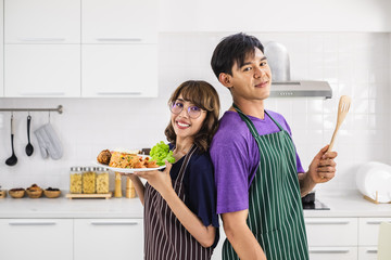 Smiling  happy young Asian couple wearing apron and cooking together in a white kitchen background