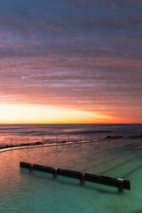 Fototapeta premium Cloudy dramatic sky view over Bronte rock pool at dawn.