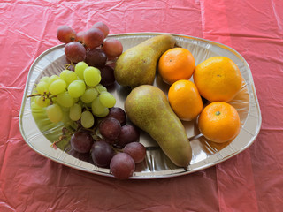 green and red grapes, a pair of pears and tangerines on a platter on a table covered with red tablecloth