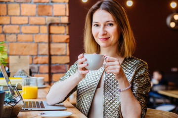 Caucasian woman blogger relaxing drinking tea while sitting with portable net-book in modern loft...
