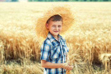 Open portrait of a little boy in a straw hat on a walk near the wheat field
