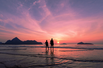 Two lovers standing together on a tropical beach,  beautiful sunset in the background