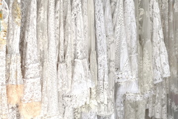Background of white lace chiffon clothes hanging on racks. Wedding dresses. Airy light summer blouses. Lacy ruffled sleeves. Female fashion.