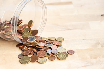 Kassensturz des Ersparten aus einem Kleingeldtopf mit vielen EURO-Münzen auf einer Tischplatte aus Holz