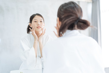 Female Skin Care. Young asian woman touching her face and looking to mirror in bathroom
