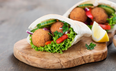 Falafel and fresh vegetables in pita bread on wooden table.