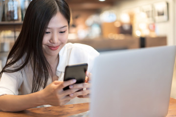 Young Asian woman using phone at a coffee shop happy and smile.