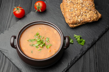 Vegetable cream soup sprinkled with parsley. Nearby are two cherry tomatoes, and two slices of bread.