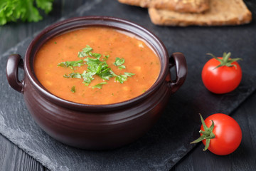 Vegetable cream soup sprinkled with parsley. Nearby are two cherry tomatoes, and two slices of bread.
