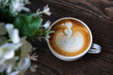 Latte art coffee on wooden table with flowers foreground