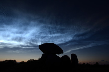 Steel blue noctiliucent clouds with the silhouette of a round barrow as foreground.