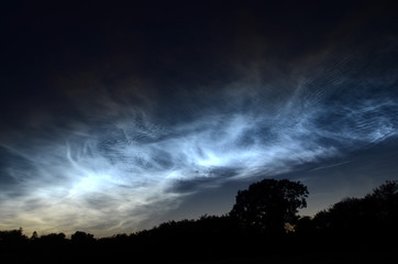 Steel blue noctiliucent clouds seen in a silhouette landscape.