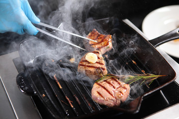 Cooking a piece of beef on the grill indoors. Cooks hands in the frame. Fillet of beef minion. The cook turns the pieces of meat with tweezers. Delicious meat from beef.