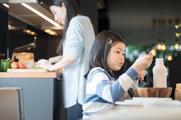 mom and daughter eating Cereals with milk having breakfast in kitchen.
