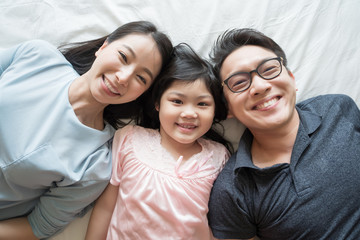 portrait of happy asian family lying on bed and looking up and holding hands
