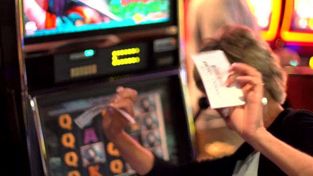 This Video Shows An Older Caucasian Woman Playing A Slot Machine And Winning.  She Celebrates Her Win And Waves Her Vouchers In The Air.