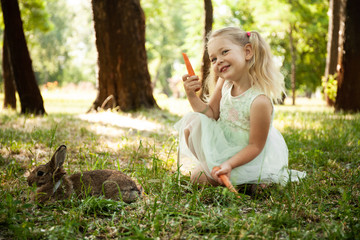 Little cute baby girl eat carrots with fluffy pet rabbit, care and living with animal. Healthy food and vegetable snack.
