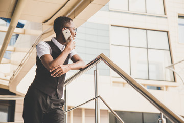 Young african american business man in suit and eyeglasses talking on the phone on the background of the business center