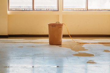 water leak drop interior office building in red bucket from Ceiling and flow on terrazzo floor