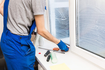 Close-up of a man in uniform and blue gloves washes a windows with window scraper. Professional...