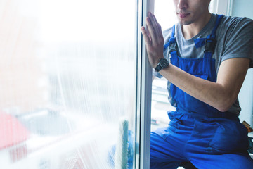 Close-up of a man in uniform and blue gloves washes a windows with window scraper. Professional...