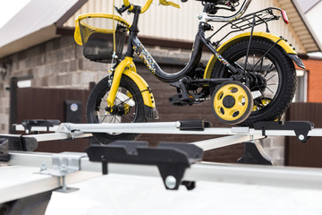 Bicycle transportation - a children's bicycle on the roof of a car against the sky in a special mount for cycling. The decision to transport large loads and travel by car