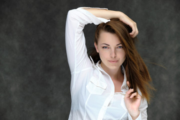Closeup portrait of pretty girl, brunette woman 30 years old on a light gray background in a white shirt with dark hair and excellent skin. She shows emotions, smiles, wonders.