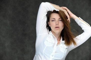 Naklejka premium Closeup portrait of pretty girl, brunette woman 30 years old on a light gray background in a white shirt with dark hair and excellent skin. She shows emotions, smiles, wonders.