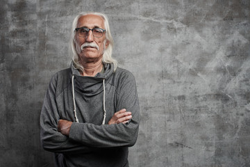Old Caucasian gray-haired cool grandfather with glasses incredulously looks into the camera with...