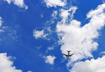 Airplane flying through the air in blue skies with some clouds and sunshine.