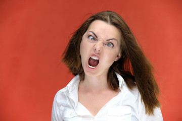 A close-up portrait of a pretty girl, a brunette woman of 30 years old on a red background in a white shirt with flowing dark hair and excellent skin. She shows emotions, smiles, wonders.
