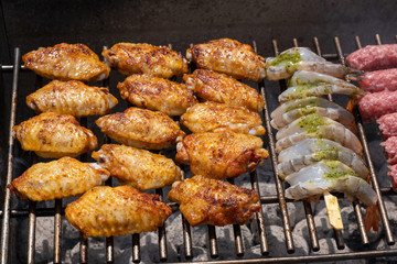 Mixed assortment of marinated meat, chicken, and prawns grilling on hot coals on a BBQ