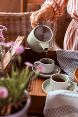 A woman pours tea into a mug of tea. Cozy atmosphere and homemade breakfast at home. Toned photo.