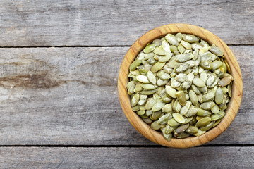 Full bowl of pumpkin seeds close up on a wooden table.