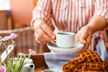 Fototapeta na wymiar Women holding a cup of tea. Homemade breakfast with waffles and coffee. Toned photo. Cozy atmosphere at home and flowers on the table.