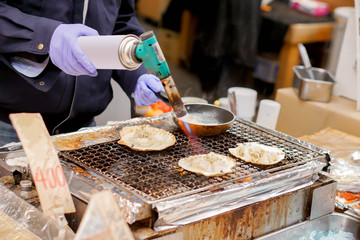 Hand of chef using burner cooking and burn big scallops shells with cheese on stove to sale for customer at Kuromon market. scallops Bar-B-Q is popular among tourists who come to the Osaka, Japan.
